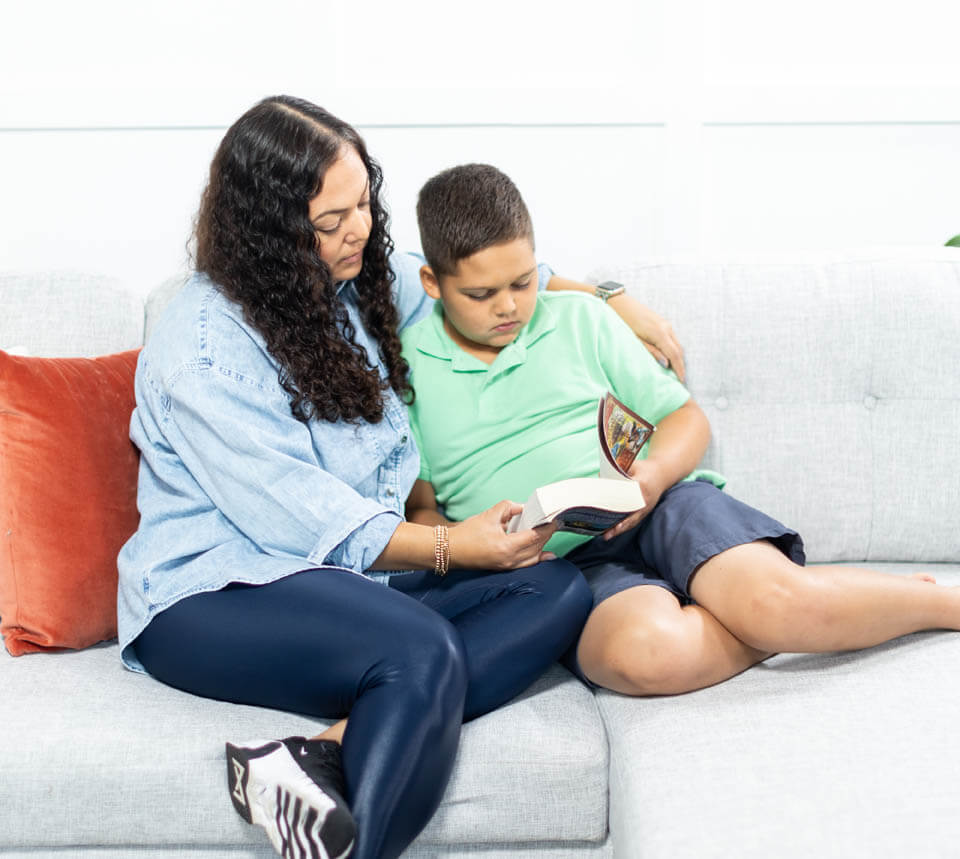 Mother with arm around son with both of them holding a book that they're reading together